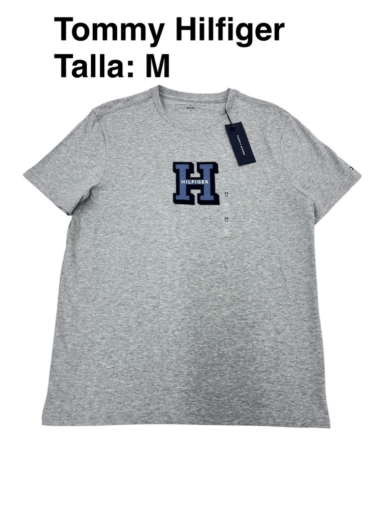 Playera Tommy Hilfiger gris con un gráfico bordado en el centro con la letra H de estilo universitario talla m